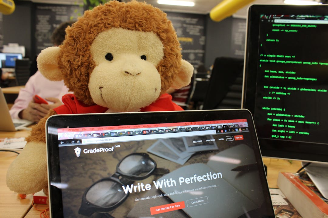 Se muestra la primera versión de gradeproof.com en una laptop. Al lado, está nuestra mascota: Gavin, el mono de GradeProof.